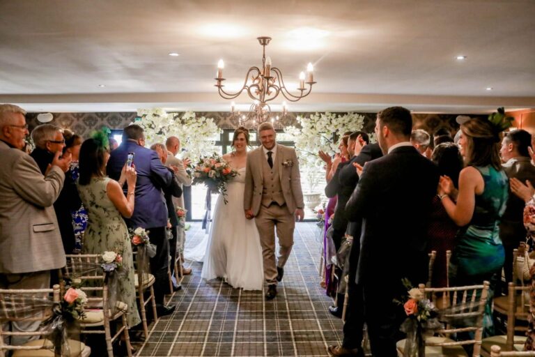 A happy bride and groom walk back down the aisle surrounded by friends and family
