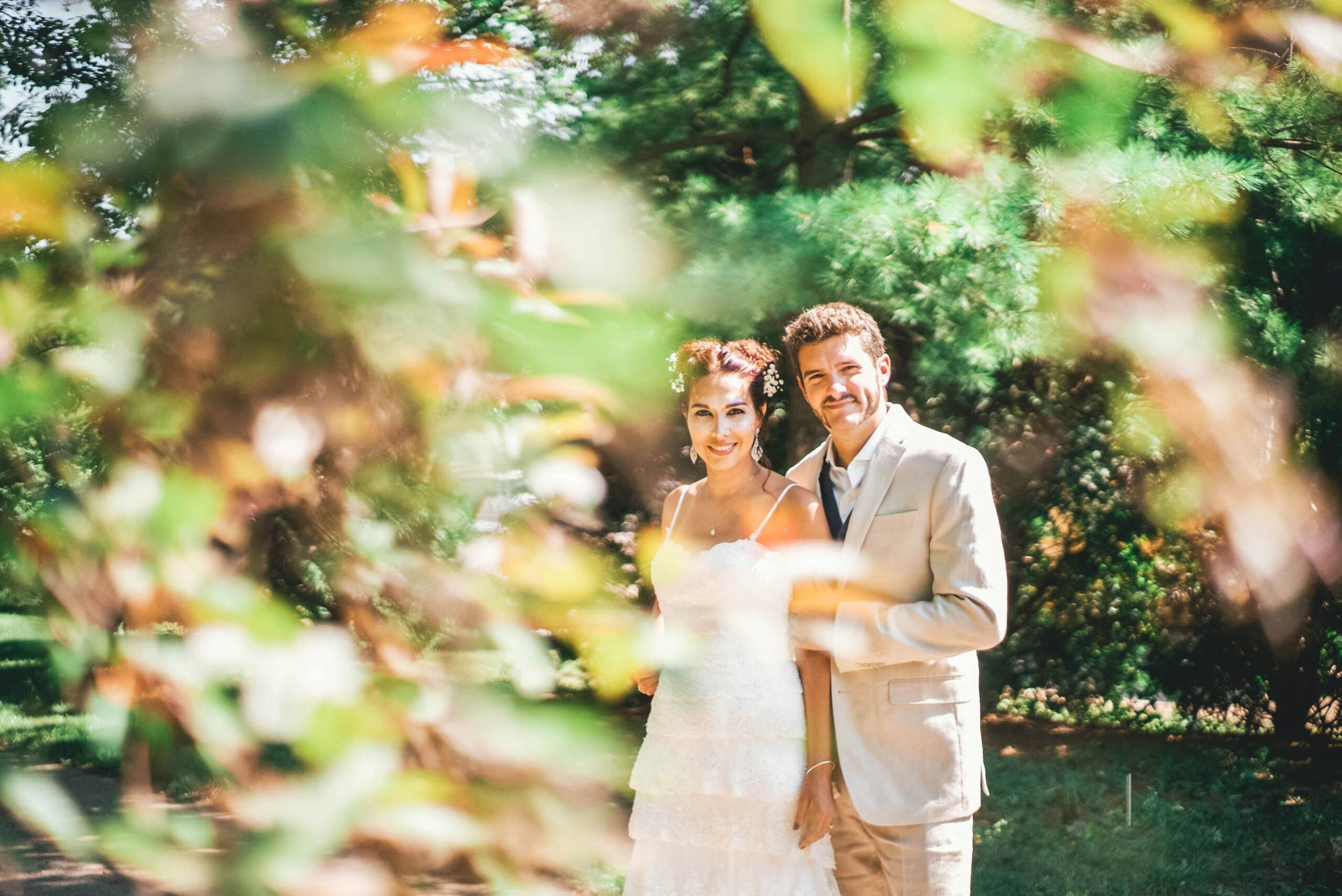 Married couple smiling at the camera through the trees on their wedding day